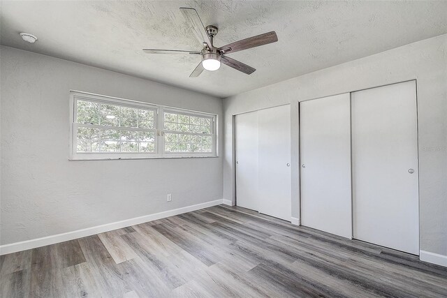 unfurnished bedroom featuring a textured ceiling, two closets, baseboards, and wood finished floors