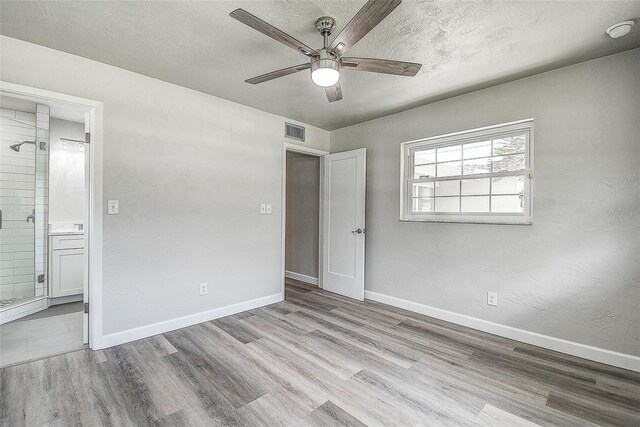 unfurnished bedroom featuring visible vents, baseboards, ensuite bathroom, wood finished floors, and a textured ceiling