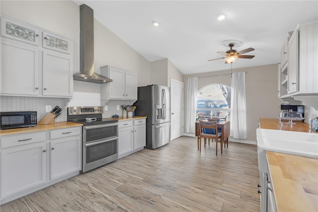 kitchen with stainless steel appliances, wooden counters, wall chimney exhaust hood, and light wood-style flooring