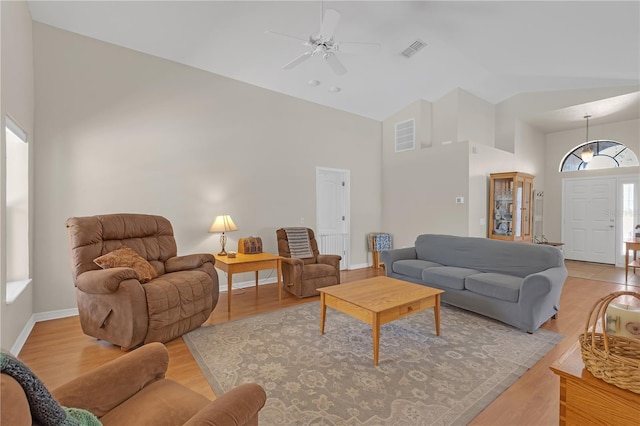 living room featuring light wood-style flooring, baseboards, visible vents, and high vaulted ceiling