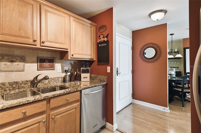 kitchen with light stone counters, light wood finished floors, a sink, stainless steel dishwasher, and backsplash