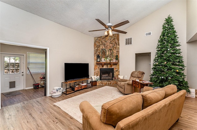 living area with a stone fireplace, light wood-style floors, visible vents, and a textured ceiling