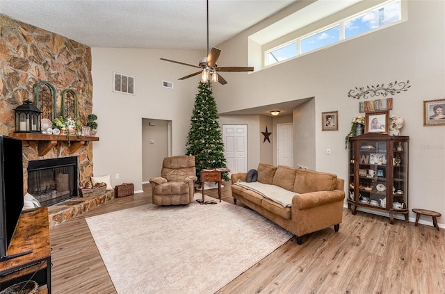 living room featuring a stone fireplace, light wood-style flooring, visible vents, and a textured ceiling