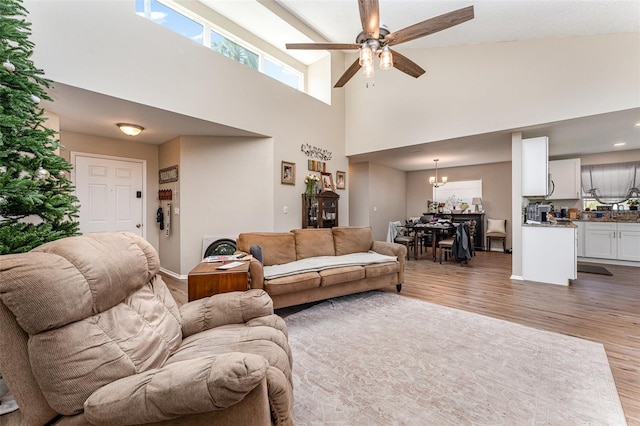 living area with ceiling fan with notable chandelier, a high ceiling, wood finished floors, and baseboards