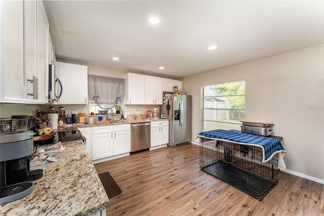 kitchen featuring light stone counters, white cabinets, stainless steel appliances, and light wood-type flooring