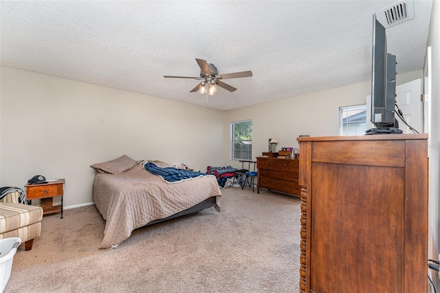 bedroom with visible vents, baseboards, light colored carpet, a textured ceiling, and a ceiling fan