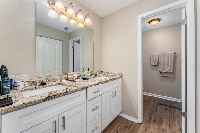 full bath featuring a sink, baseboards, wood finished floors, and double vanity