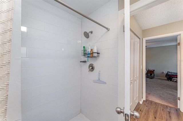 full bath with a tile shower, a textured ceiling, and wood finished floors