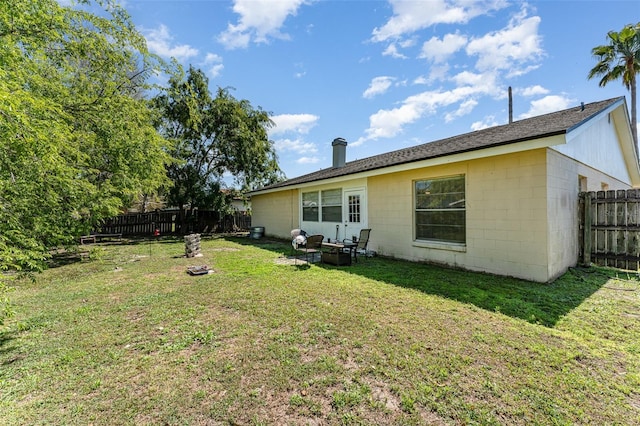 rear view of house with concrete block siding, a yard, and a fenced backyard