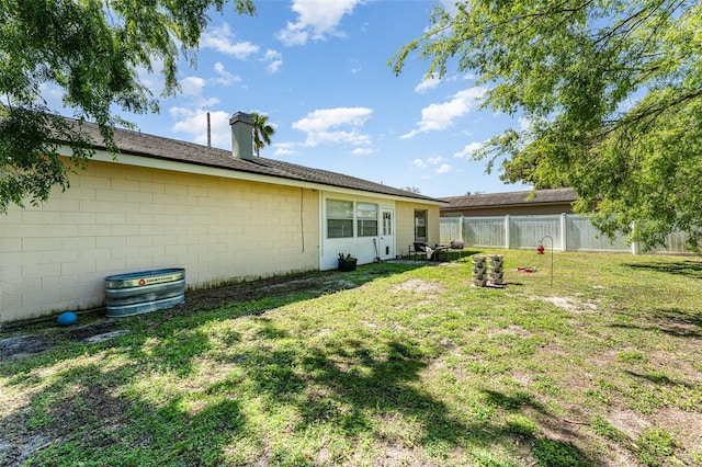 rear view of house with a lawn, concrete block siding, a chimney, and fence