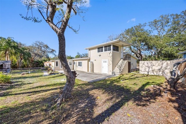 back of house with stucco siding, a lawn, fence, stairway, and a patio area