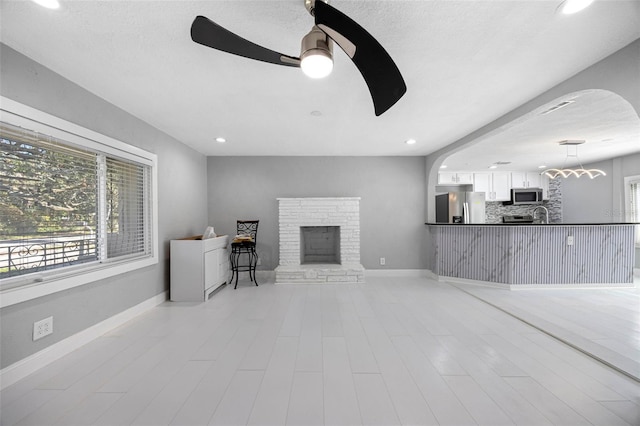 living room with a fireplace with raised hearth, a textured ceiling, recessed lighting, baseboards, and ceiling fan