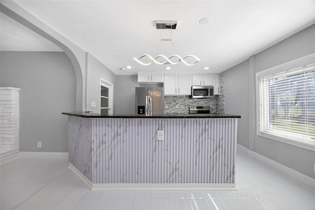 kitchen featuring arched walkways, stainless steel appliances, white cabinetry, dark countertops, and backsplash