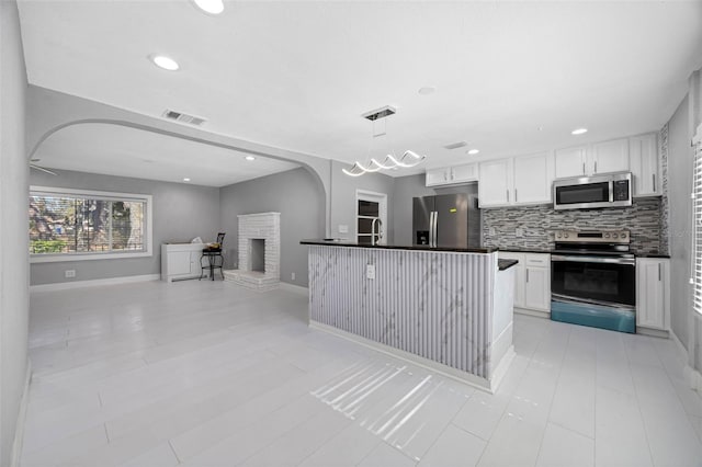 kitchen featuring dark countertops, open floor plan, arched walkways, appliances with stainless steel finishes, and decorative backsplash