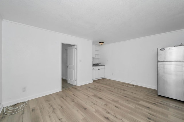 interior space featuring light wood-type flooring, baseboards, a textured ceiling, and crown molding