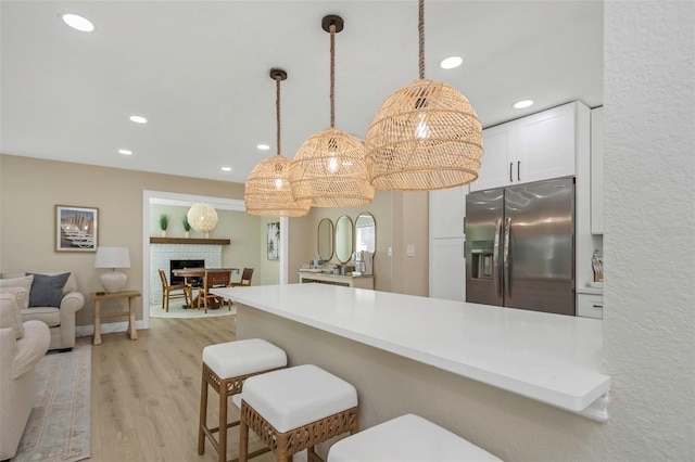 kitchen featuring light wood-style flooring, stainless steel fridge with ice dispenser, white cabinets, pendant lighting, and open floor plan