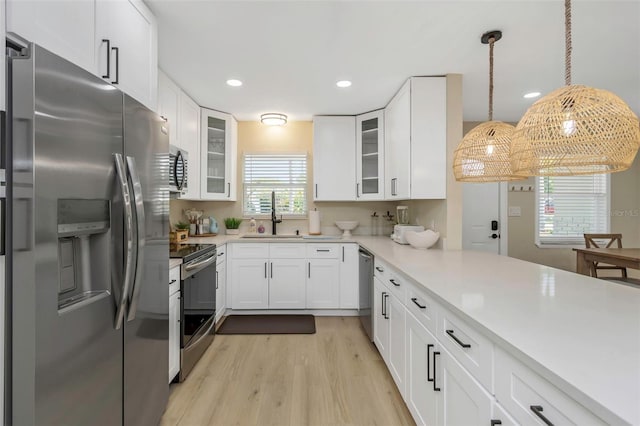 kitchen with a sink, white cabinetry, stainless steel appliances, light wood-style floors, and light countertops