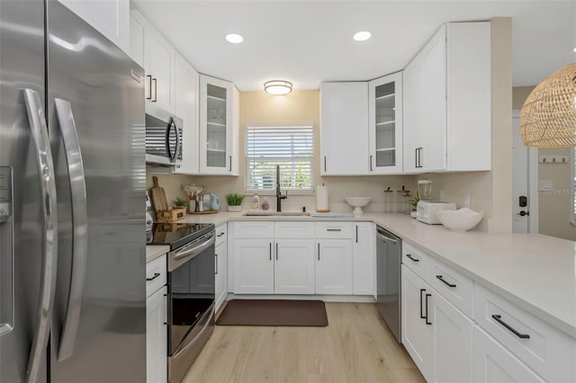 kitchen featuring light wood-type flooring, a sink, white cabinetry, appliances with stainless steel finishes, and light countertops