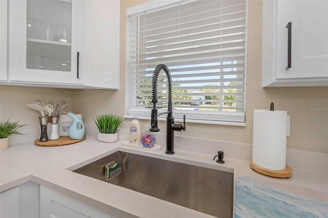 interior details with light countertops, white cabinets, glass insert cabinets, and a sink