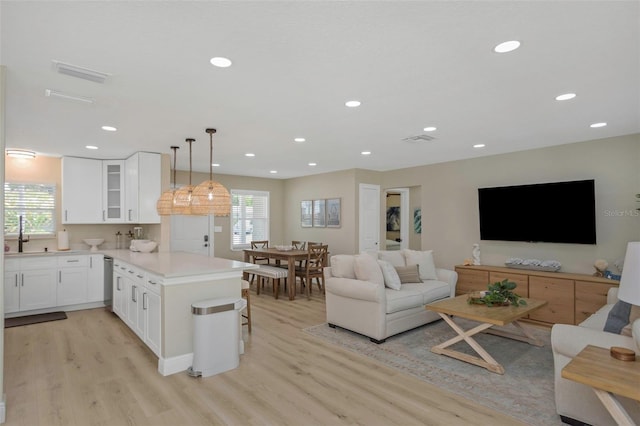 kitchen featuring visible vents, a peninsula, light wood-style flooring, glass insert cabinets, and open floor plan