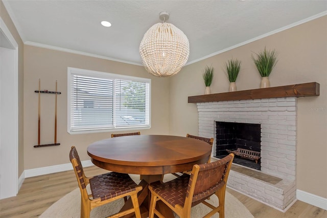 dining area featuring baseboards, light wood finished floors, an inviting chandelier, a fireplace, and crown molding