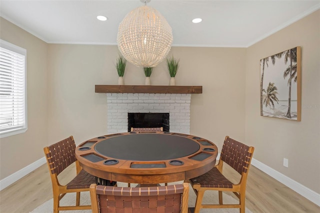 dining space with wood finished floors, baseboards, a brick fireplace, and ornamental molding