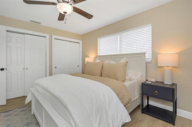 bedroom featuring visible vents, baseboards, multiple closets, and wood finished floors