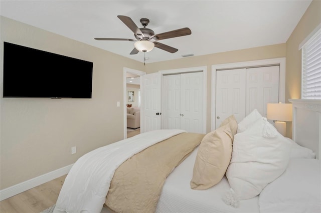 bedroom featuring wood finished floors, visible vents, baseboards, ceiling fan, and multiple closets