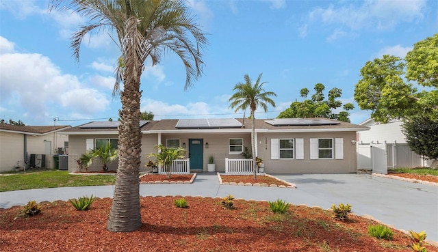 single story home with central air condition unit, roof mounted solar panels, covered porch, and fence