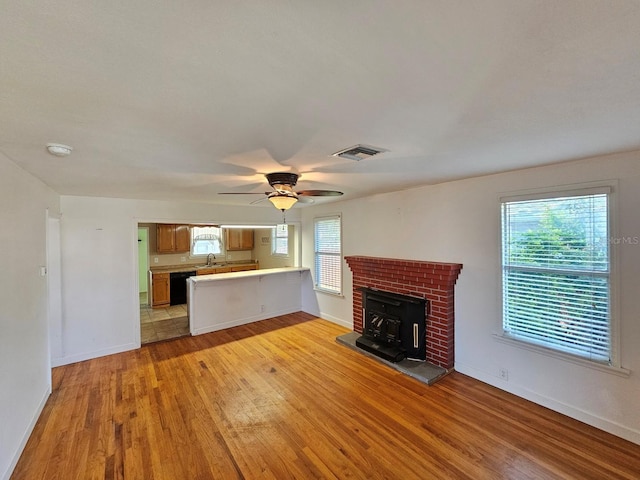 unfurnished living room with light wood finished floors, visible vents, baseboards, a wood stove, and a sink