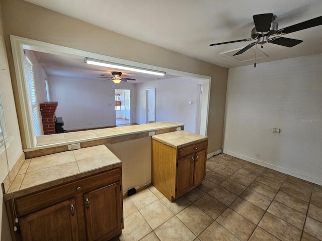 kitchen with light tile patterned floors, a ceiling fan, a peninsula, a wood stove, and tile counters