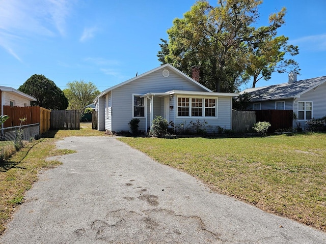 view of front of property with driveway, a chimney, a front lawn, and fence