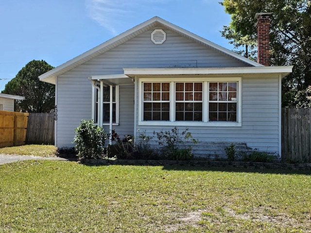 bungalow-style home with a chimney, a front yard, and fence