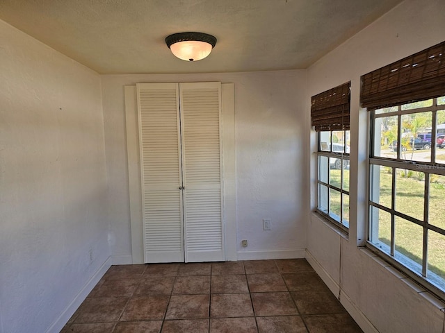 unfurnished bedroom featuring a closet, a textured wall, baseboards, and dark tile patterned flooring