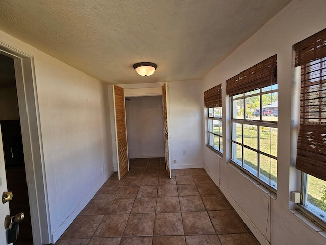 interior space with dark tile patterned flooring, baseboards, a closet, and a textured ceiling