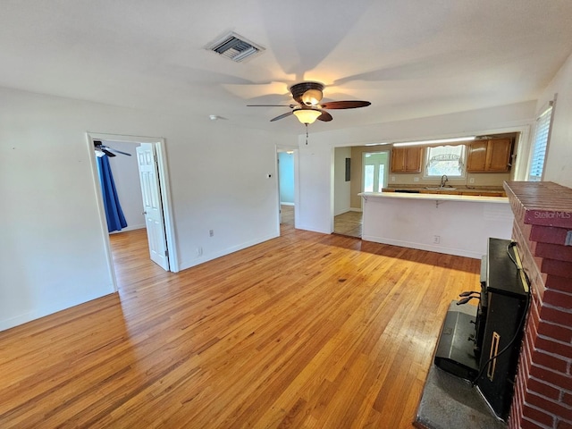 unfurnished living room with visible vents, a sink, light wood-style floors, baseboards, and ceiling fan