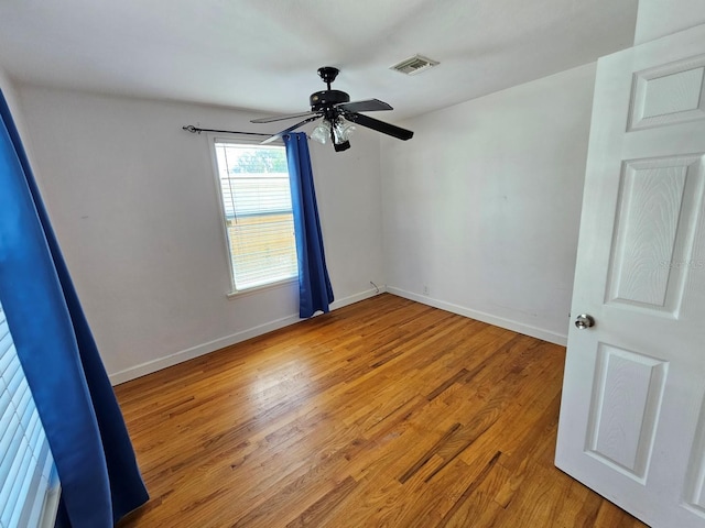 spare room featuring a ceiling fan, visible vents, light wood finished floors, and baseboards