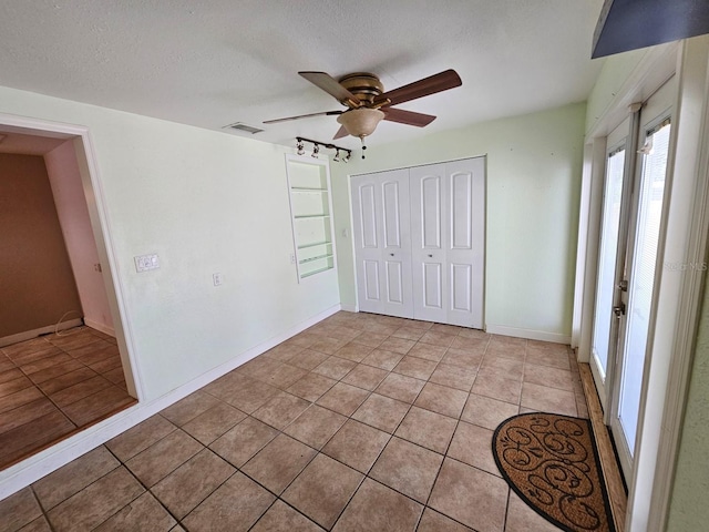 unfurnished bedroom with visible vents, light tile patterned floors, a closet, a textured ceiling, and a ceiling fan