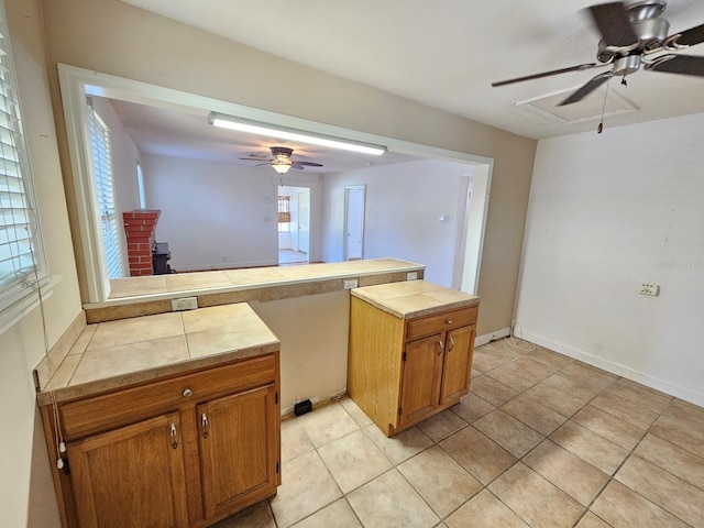 kitchen featuring light tile patterned floors, a ceiling fan, a peninsula, a wood stove, and brown cabinets