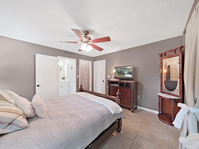 bedroom with light tile patterned floors, a ceiling fan, baseboards, ensuite bathroom, and a textured ceiling