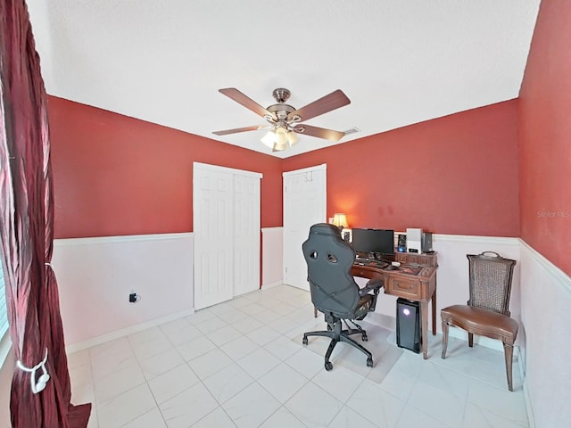 tiled office space featuring visible vents, wainscoting, and ceiling fan