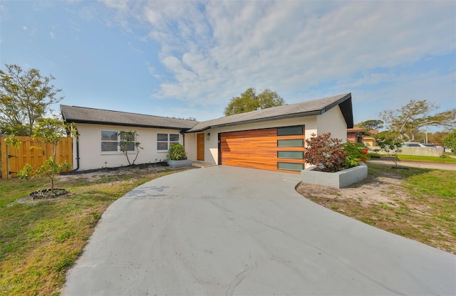 view of front of house featuring stucco siding, driveway, an attached garage, and fence