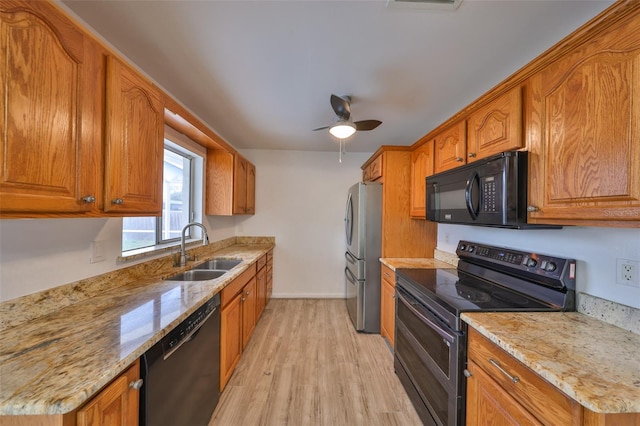 kitchen with brown cabinetry, black appliances, light wood-type flooring, and a sink