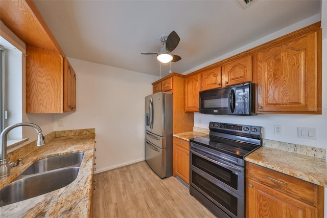 kitchen featuring a sink, stainless steel appliances, light wood-style floors, brown cabinetry, and light stone countertops