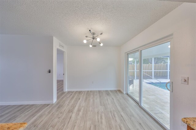 unfurnished room with visible vents, baseboards, light wood-style flooring, a textured ceiling, and a notable chandelier