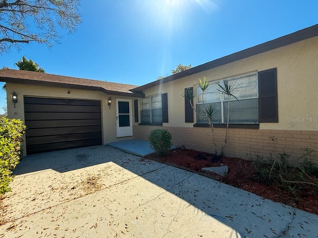 ranch-style home with brick siding, stucco siding, driveway, and an attached garage