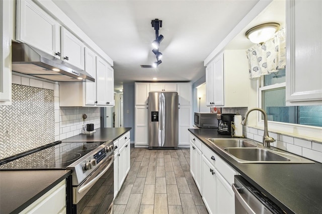 kitchen with a sink, under cabinet range hood, appliances with stainless steel finishes, white cabinetry, and dark countertops