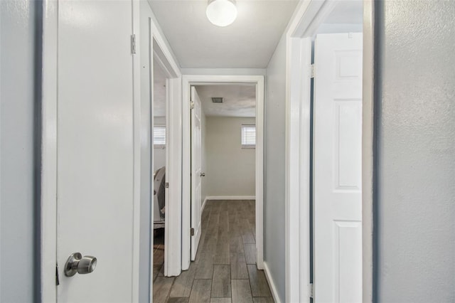 hall with baseboards, visible vents, and wood finish floors