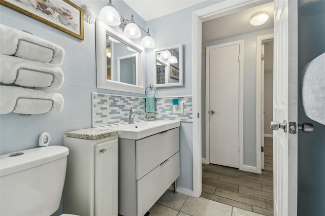 bathroom with decorative backsplash, toilet, vanity, and baseboards