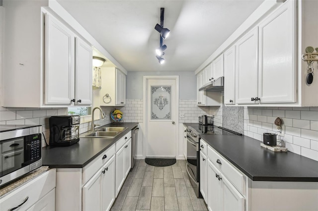 kitchen with a sink, stainless steel appliances, white cabinets, under cabinet range hood, and dark countertops